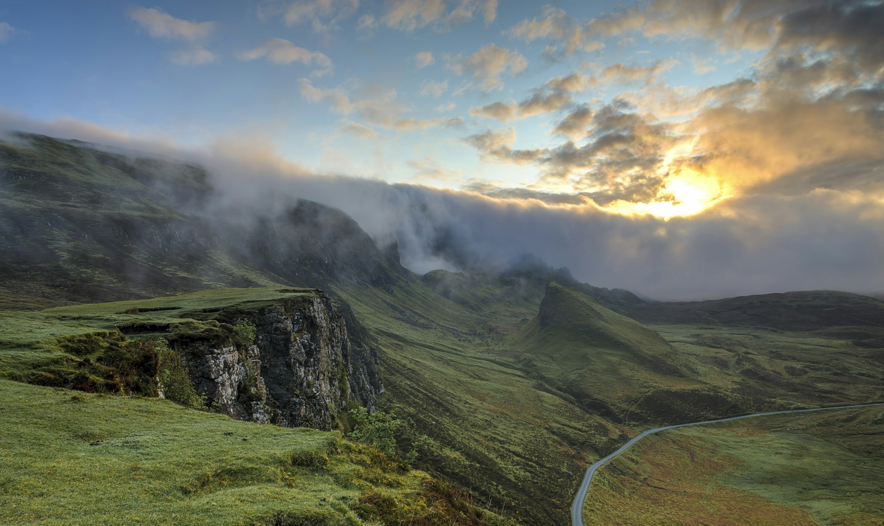 A person standing on a misty mountain ridge at sunrise, overlooking a valley